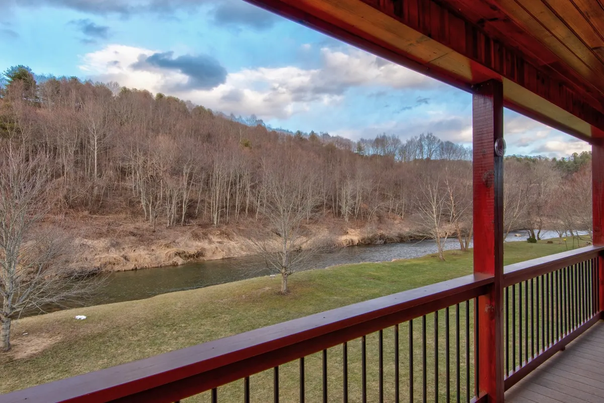 This image captures a tranquil riverside scene featuring a gently flowing river framed by bare trees, with mountains visible in the background. The setting is open and natural, inviting outdoor exploration and relaxation beside the water.