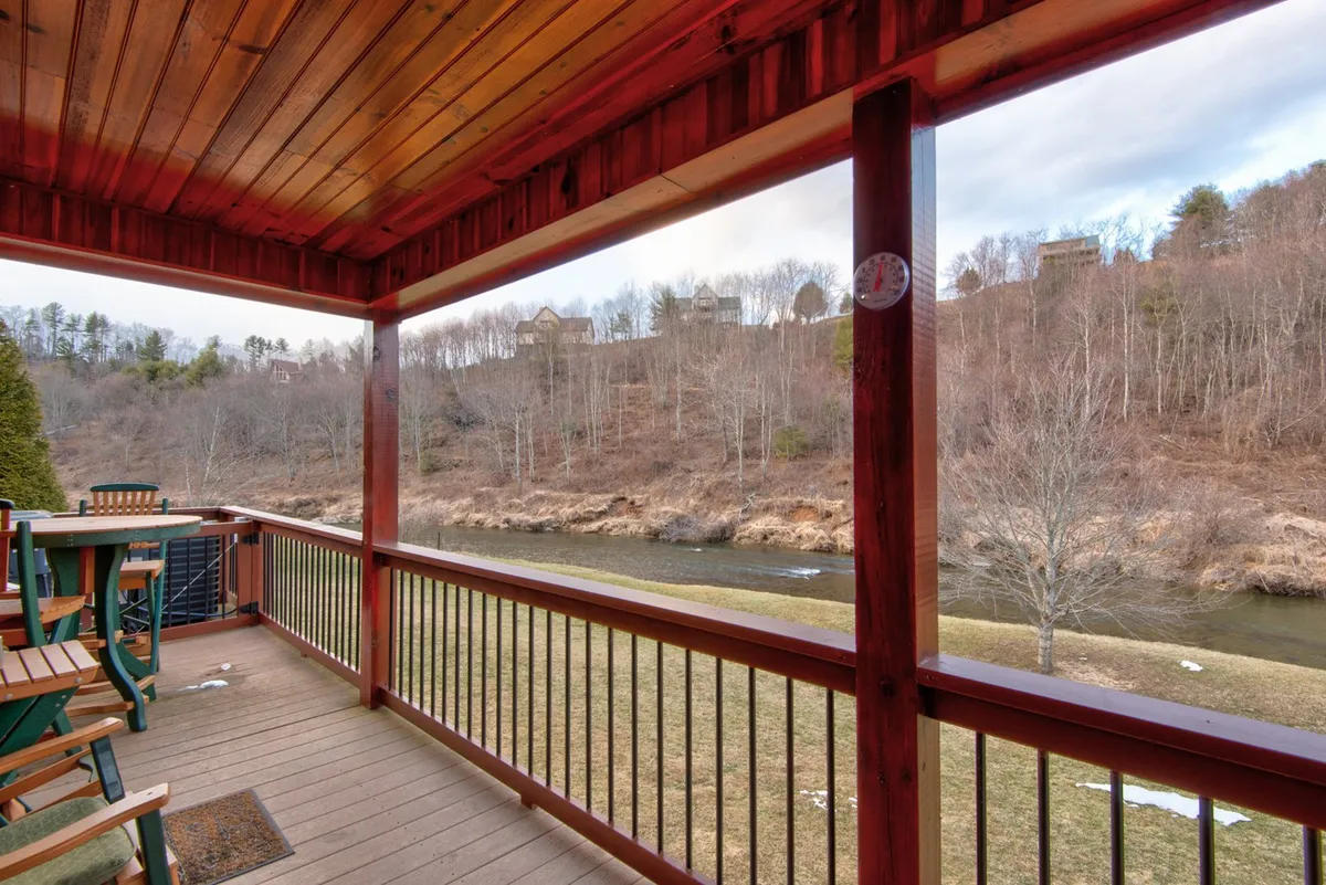 A wooden deck overlooks the river, surrounded by lush trees. The space is ideal for relaxing, socializing, and watching wildlife, offering a seamless connection between the home and the natural environment.
