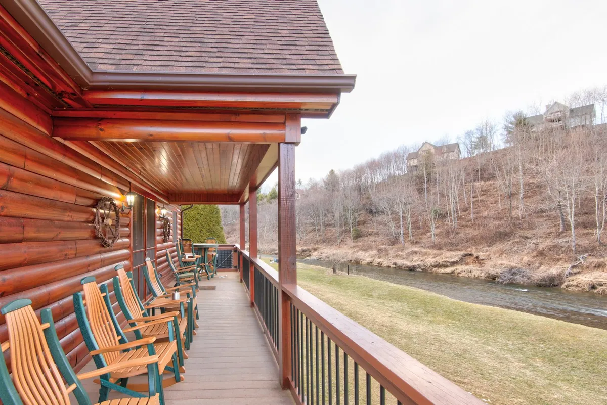 A close-up of the porch with classic rocking chairs and a wooden railing, overlooking a serene river view. The tranquil scene emphasizes relaxation and the soothing presence of the river, perfect for morning coffee or evening gatherings.