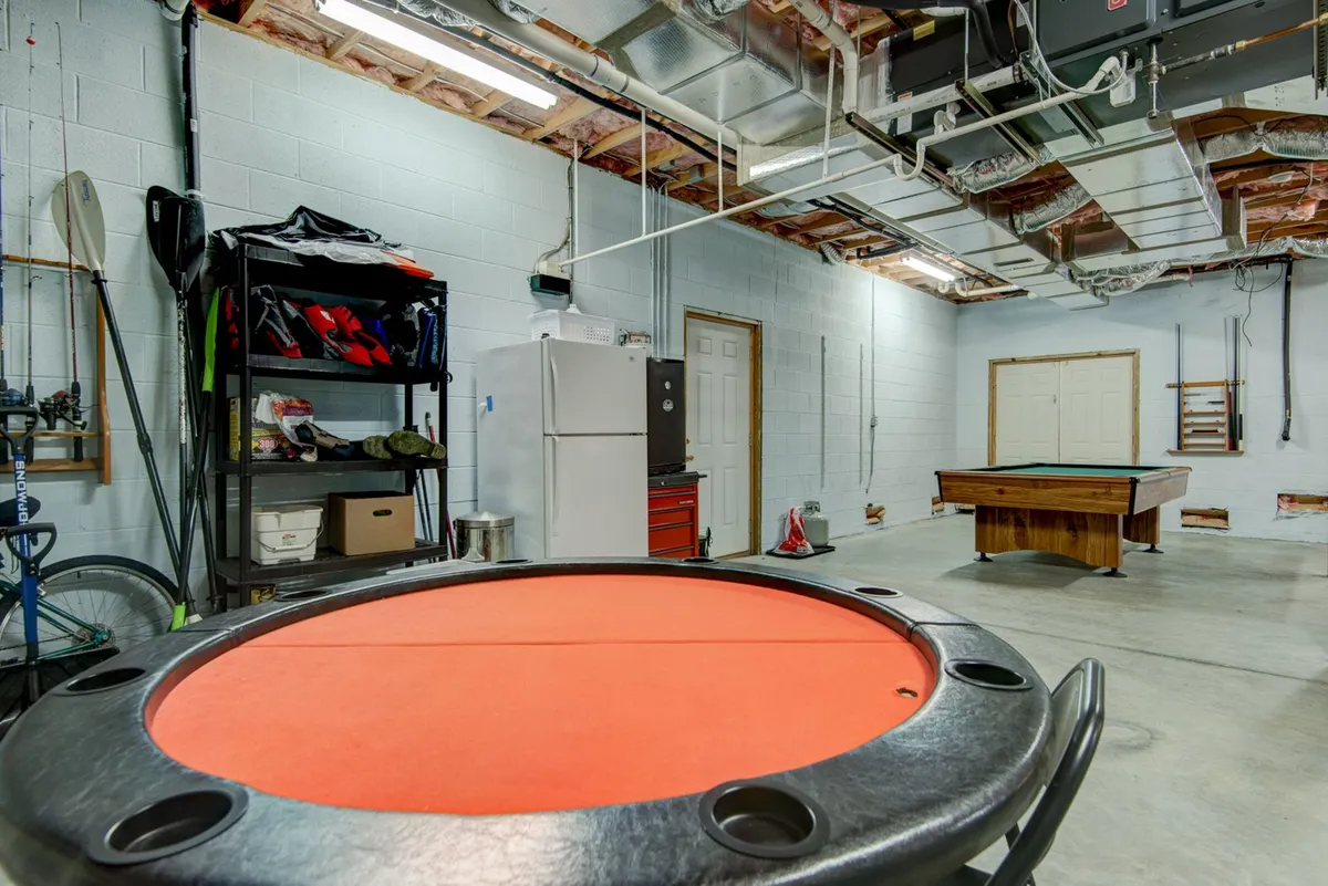 This image captures the heart of the game room, with a poker table and pool table as focal points. A refrigerator and shelving with equipment are visible, reinforcing the entertainment-focused atmosphere. The setting is lively but relaxed, well-suited for social gatherings or friendly competitions.