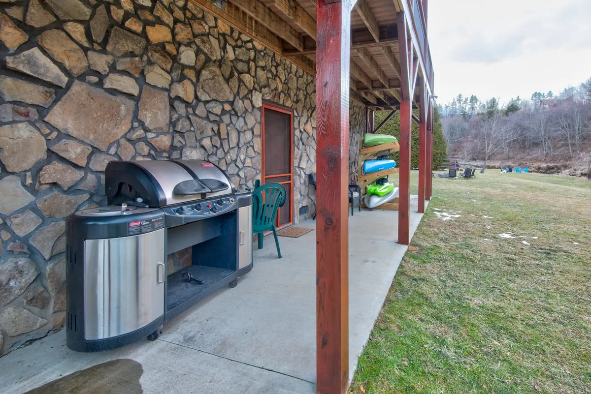 This image features a welcoming outdoor space with a grill, a green chair, and a visible stack of kayaks, evoking a sense of outdoor leisure and group gatherings. The setting hints at the possibility of barbecues, yard games, and riverside relaxation, connecting to the communal, activity-focused narrative of the section.