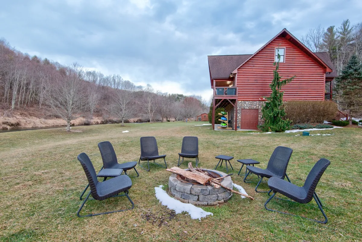 A cozy fire pit area with comfortable seating is nestled in the yard, with the house structure and natural landscape in the background. The setting is ideal for group gatherings, storytelling, and stargazing under the open sky.