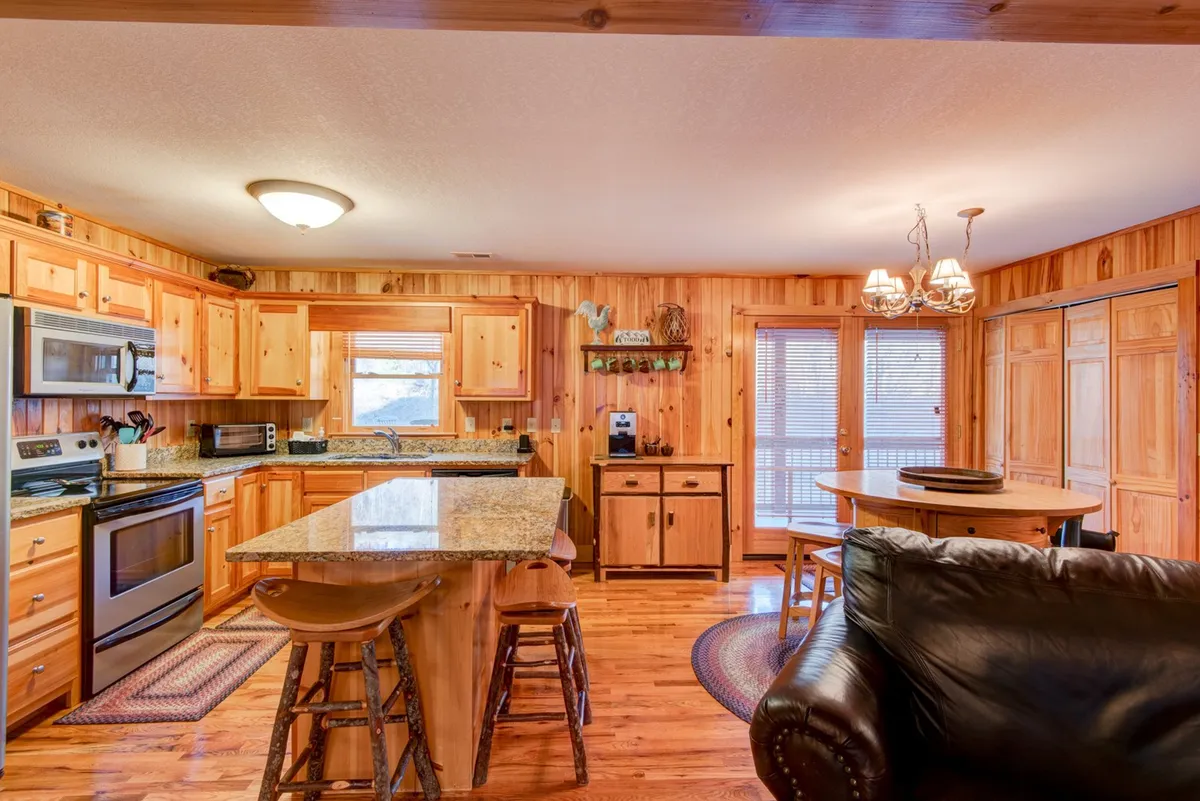 A bright, welcoming kitchen with a granite island, rich wood cabinetry, and an open view to a dining area. Large windows flood the space with natural light, creating a perfect spot for cooking, casual dining, and entertaining guests.
